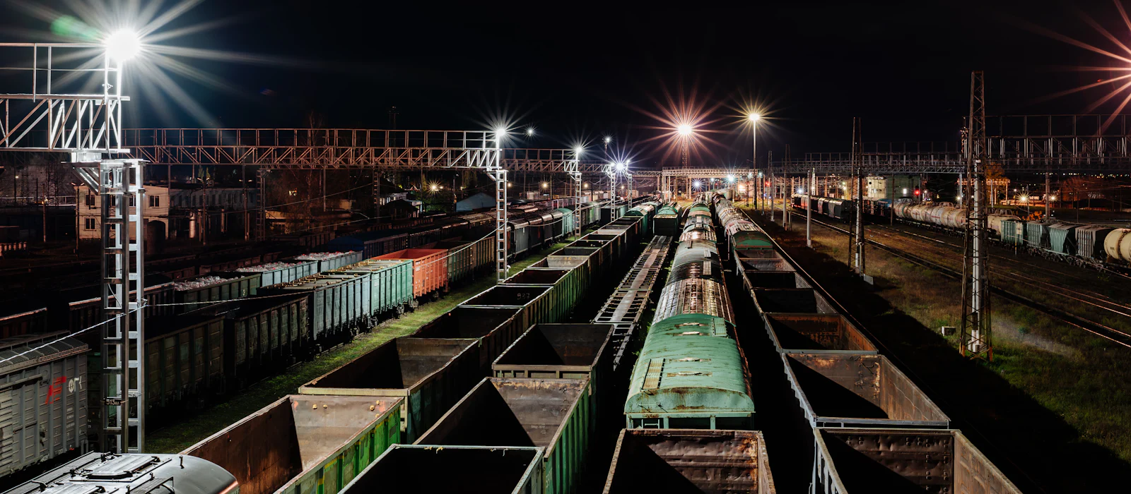 A classification yard at night: rows of freight cars held on parallel tracks under mast lights.